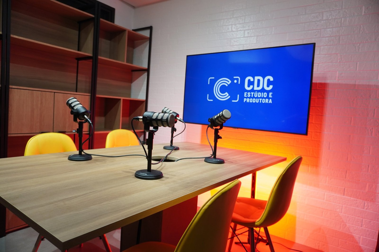 Estúdio da CDC com iluminação laranja e quatro microfones na mesa